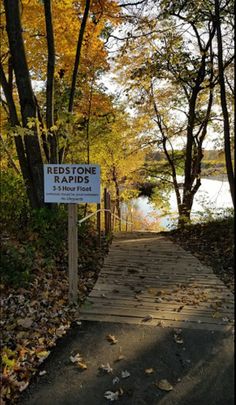 a sign that is on the side of a wooden path near some trees and leaves