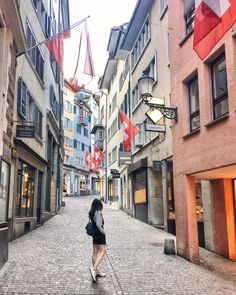 a woman is walking down the street in an old european city with flags hanging from buildings