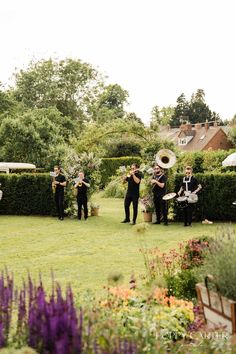 a group of people standing on top of a lush green field next to a garden