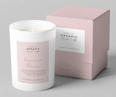 a white candle sitting next to a pink box on a gray surface with the label organic beauty