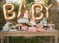 a table topped with lots of cake next to a giant balloon that says'baby '