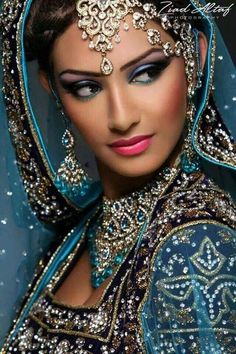 a woman wearing a blue veil and headpiece with jewels on her face is looking at the camera