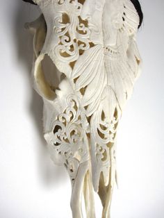 an intricately carved cow skull hanging on the wall in front of a white background