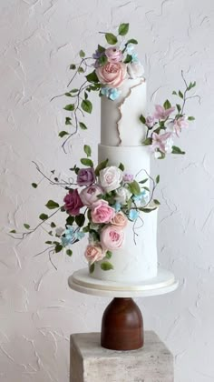 a three tiered white cake with flowers on top and greenery around the edges