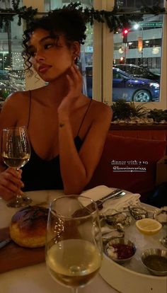 a woman sitting at a table in front of a glass of wine and donut