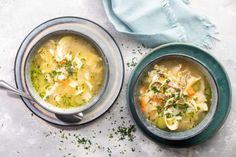 two bowls of chicken noodle soup on a white table with a blue towel and napkin