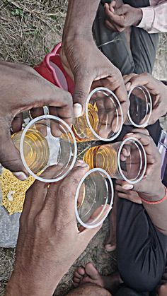 several people are holding glasses with drinks in each others hands while sitting on the ground