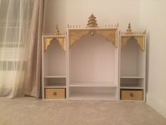 a white shelf with two yellow drawers and gold trimmings on the top, in front of a beige curtained window