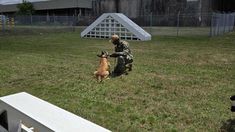 a man kneeling down next to a dog on top of a grass covered field in front of a building