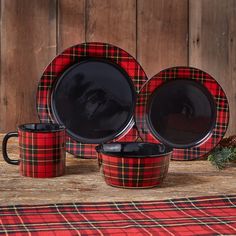 a red and black plaid table setting with two mugs, one bowl and one plate