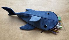 a blue fish shaped pencil case sitting on top of a wooden table next to pens and markers