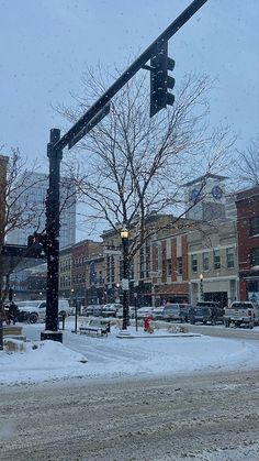 a street light on a snowy day in the winter with buildings and cars behind it