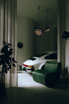 a white car parked in front of a window next to a green chair and potted plant