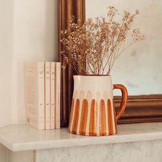 an orange and white vase sitting on top of a mantle next to a mirror with books