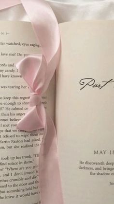 an open book with a pink ribbon tied around the page and some words written on it