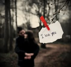 a man and woman standing in the woods with a sign that says i love you