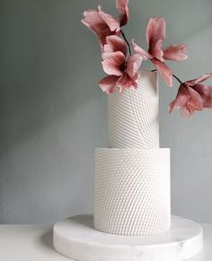 there is a white cake with pink flowers in it on the table next to a gray wall