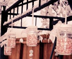 mason jars filled with pink and white beads hanging from a wooden beam in front of snow covered trees