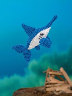 a blue and white crocheted shark kite is flying in the sky above a wooden structure