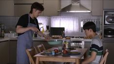 two young men are preparing food in the kitchen while one man is standing at the table