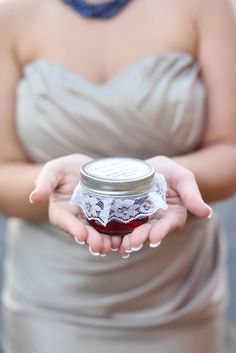 a woman in a gray dress holding a jar of jam with lace on the bottom