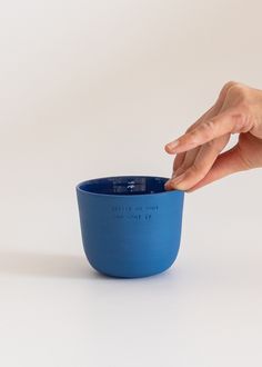 a hand reaching into a blue bowl with writing on the inside and outside, against a white background