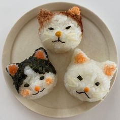 three sushi rolls decorated to look like cats with orange noses and tails on a white plate