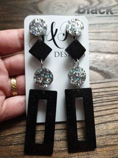 a pair of black and white earrings on top of a wooden table next to a card