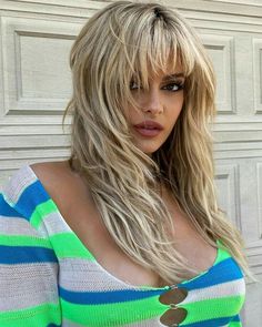 a woman with long blonde hair wearing a green and blue striped shirt is standing in front of a garage door