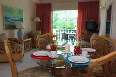 a glass table with plates and cups on it in front of a television set that has red curtains