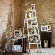 a white ladder with pictures and flowers on it in front of a stone wall next to other items