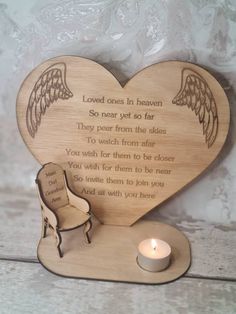 a heart shaped wooden plaque with an angel wing on it and a lit candle next to it