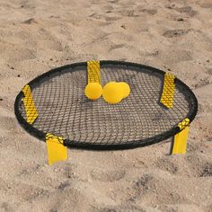 a tennis net with two yellow balls on it in the middle of some sand at the beach