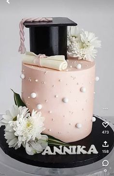 a pink cake with white flowers and a black hat on top is decorated with an inscription annika