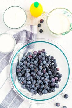 blueberries in a glass bowl next to two glasses of milk