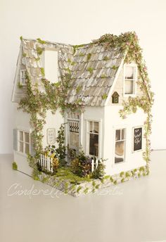 a white doll house with ivy growing on the roof and windows, in front of a white wall