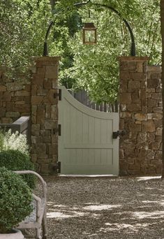 an open gate in the middle of a stone driveway with trees and bushes around it