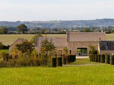 a large house in the middle of a lush green field with trees and bushes surrounding it