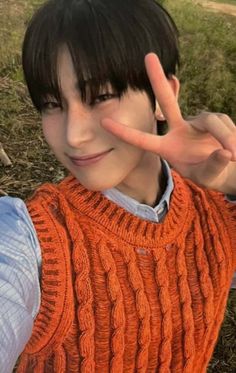 a young boy making the peace sign with his hand in front of him and an orange sweater on