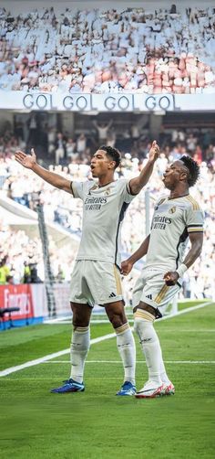 two soccer players standing on the field with their arms in the air and looking up