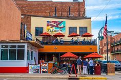 people are standing in front of a restaurant with red umbrellas on the roof and an american flag flying above it