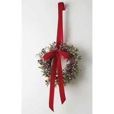 a christmas wreath hanging on the wall with a red ribbon tied around it and flowers