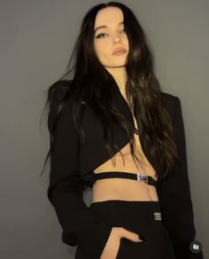 a woman with long hair wearing a black suit and posing in front of a gray background