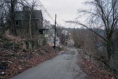 an empty road in the middle of a wooded area with houses on either side and power lines above it