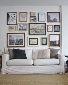 a living room filled with lots of framed pictures on the wall above a white couch