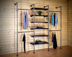 a room with wooden walls and shelves filled with clothing hanging on hooks, shoes and shirts