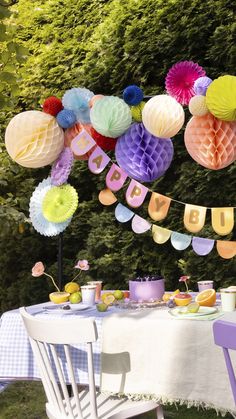 a table topped with lots of colorful paper lanterns and plates filled with food next to trees