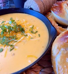 a bowl of cheese soup with bread rolls in the background