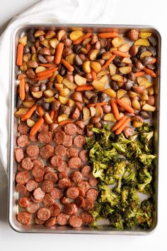 a pan filled with sausage and broccoli next to a wooden spoon on a white surface