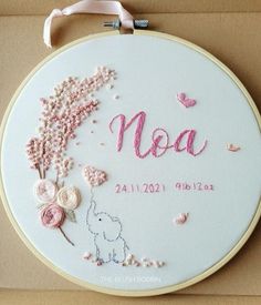 a white embroidered hoop with pink flowers and the word noa on it in cursive writing